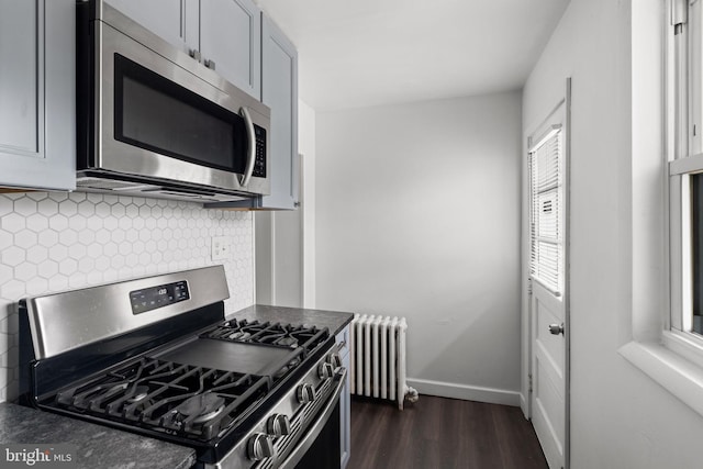 kitchen featuring dark hardwood / wood-style floors, tasteful backsplash, gray cabinetry, appliances with stainless steel finishes, and radiator heating unit