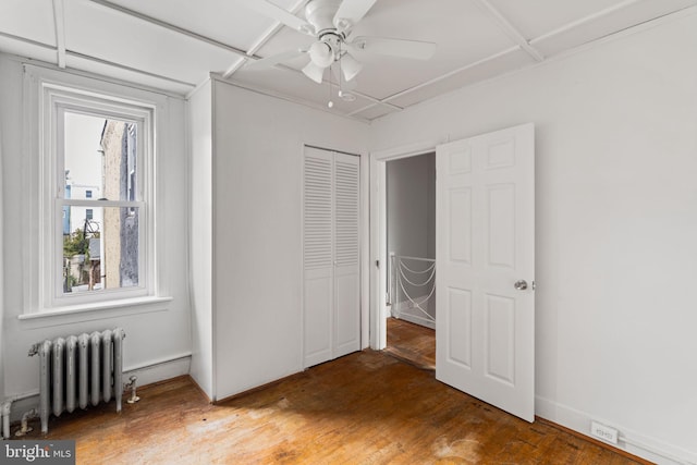 unfurnished bedroom featuring radiator, ceiling fan, a closet, and hardwood / wood-style flooring