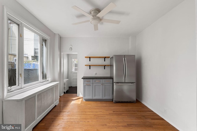 kitchen featuring light wood-type flooring, gray cabinetry, radiator, ceiling fan, and stainless steel fridge