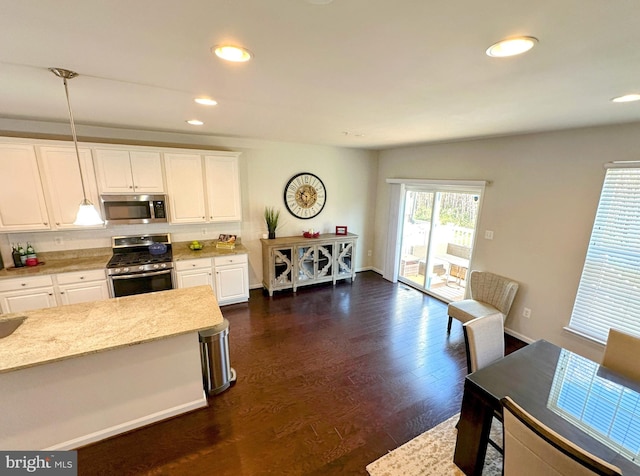 kitchen featuring white cabinetry, stainless steel appliances, light stone counters, dark hardwood / wood-style flooring, and decorative light fixtures