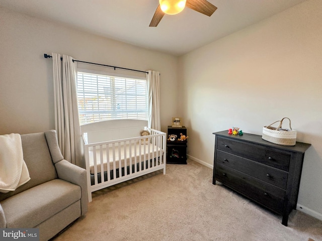 bedroom with a crib, light colored carpet, and ceiling fan