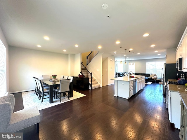 kitchen featuring stainless steel appliances, dark wood-type flooring, decorative light fixtures, a center island with sink, and white cabinets