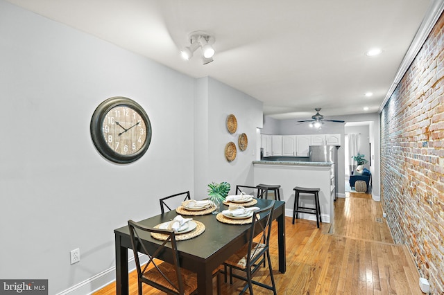 dining area with light wood-type flooring, brick wall, and ceiling fan