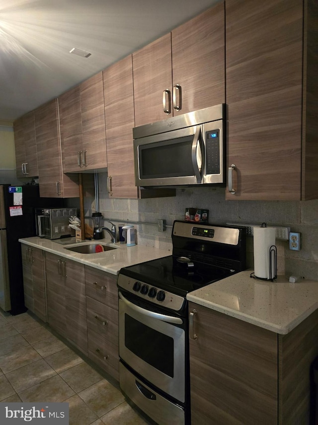 kitchen with sink, light tile patterned floors, appliances with stainless steel finishes, tasteful backsplash, and light stone counters