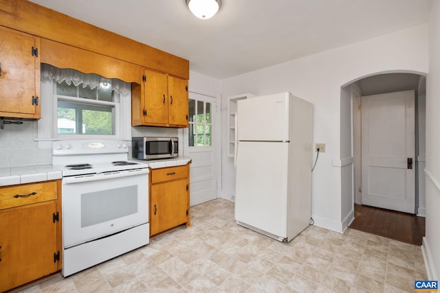 kitchen with a healthy amount of sunlight, white appliances, tile countertops, and tasteful backsplash