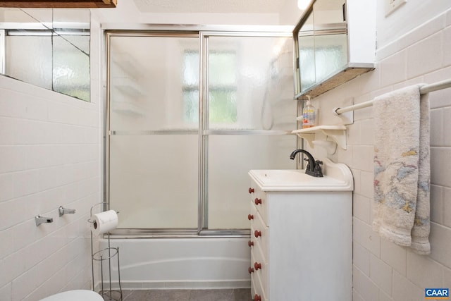 full bathroom featuring tile walls, shower / bath combination with glass door, vanity, and toilet