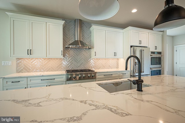 kitchen featuring appliances with stainless steel finishes, white cabinetry, sink, and wall chimney range hood