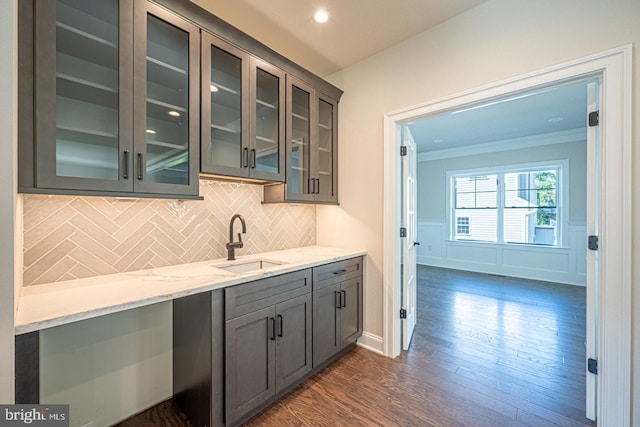 bar with light stone counters, tasteful backsplash, sink, dark hardwood / wood-style flooring, and ornamental molding