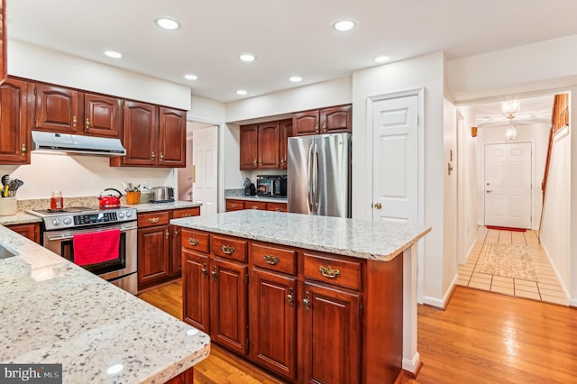 kitchen with stainless steel appliances, light stone countertops, light hardwood / wood-style floors, and a kitchen island