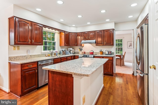 kitchen featuring light stone countertops, hardwood / wood-style floors, a center island, stainless steel appliances, and sink