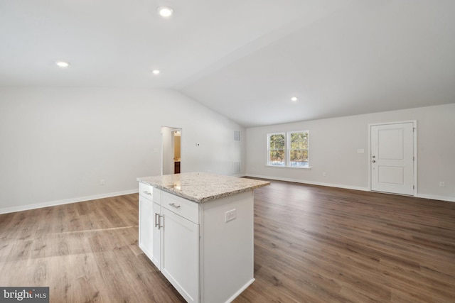 kitchen featuring white cabinets, light hardwood / wood-style flooring, vaulted ceiling, a kitchen island, and light stone counters