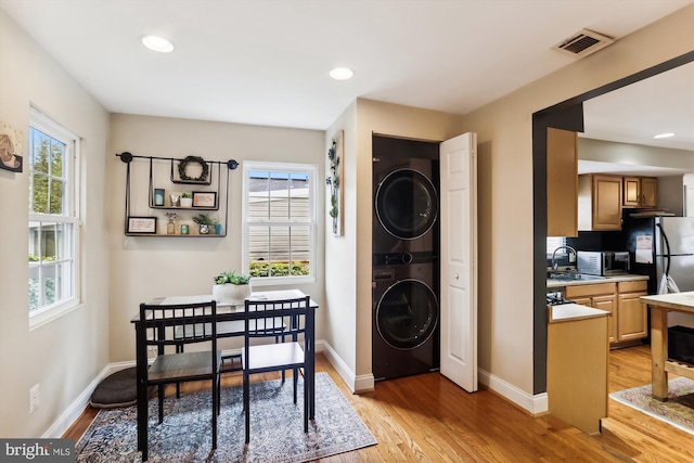 office area featuring stacked washer / drying machine, light wood-type flooring, sink, and a wealth of natural light