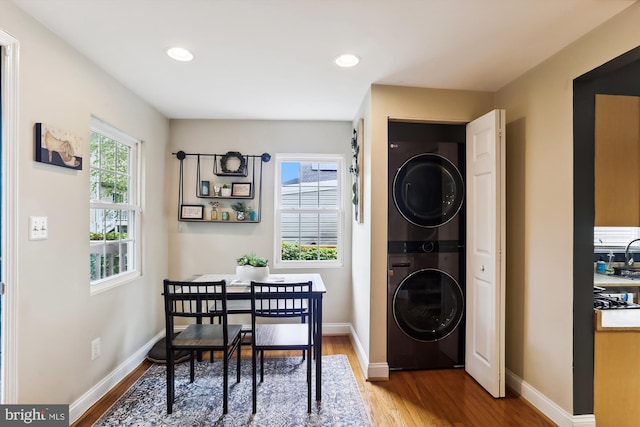 laundry area featuring stacked washer / drying machine, a healthy amount of sunlight, and wood-type flooring