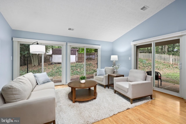 living room featuring light wood-type flooring, a textured ceiling, and high vaulted ceiling