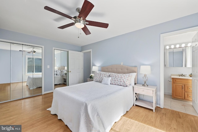 bedroom featuring light hardwood / wood-style floors, sink, ensuite bath, two closets, and ceiling fan