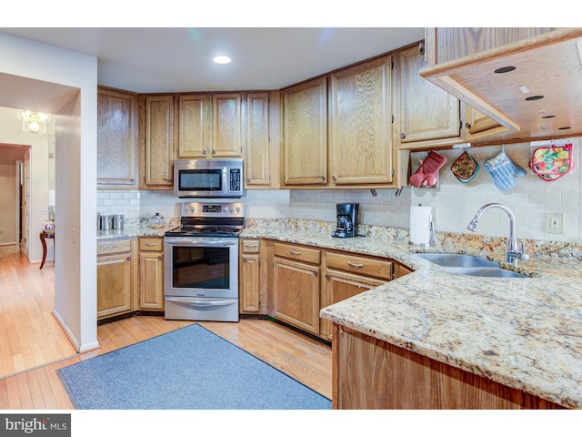 kitchen with appliances with stainless steel finishes, backsplash, light stone countertops, light wood-type flooring, and sink