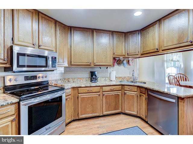 kitchen with light stone counters, sink, kitchen peninsula, appliances with stainless steel finishes, and light wood-type flooring