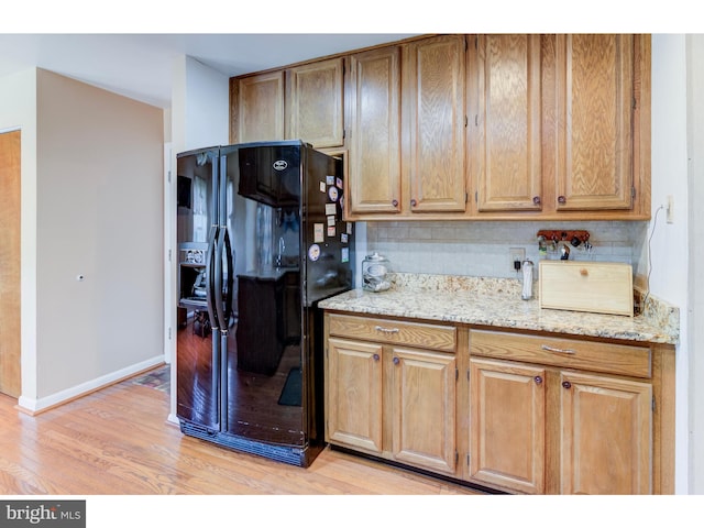 kitchen featuring light hardwood / wood-style flooring, backsplash, black fridge with ice dispenser, and light stone counters