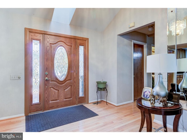 foyer entrance with light wood-type flooring, a chandelier, and vaulted ceiling