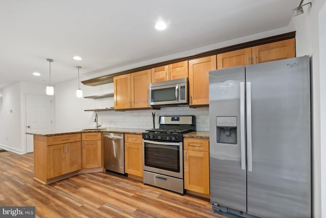 kitchen featuring wood-type flooring, pendant lighting, stainless steel appliances, and light stone counters