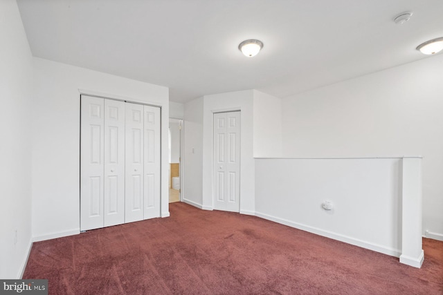 unfurnished bedroom featuring dark carpet and two closets