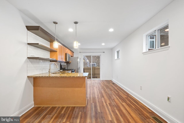 kitchen featuring hanging light fixtures, kitchen peninsula, tasteful backsplash, dark wood-type flooring, and appliances with stainless steel finishes