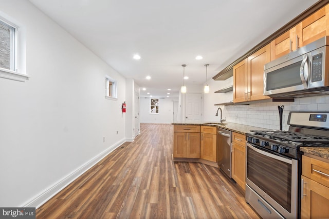 kitchen featuring pendant lighting, kitchen peninsula, stainless steel appliances, dark stone counters, and dark hardwood / wood-style flooring