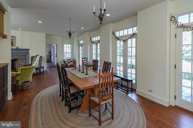 dining area with dark wood-type flooring, an inviting chandelier, and a brick fireplace