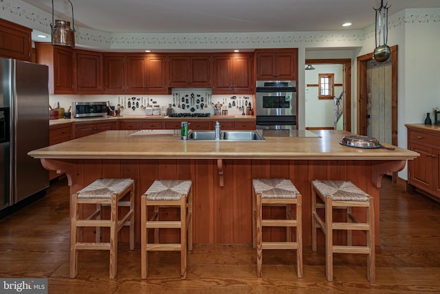 kitchen featuring dark hardwood / wood-style floors, appliances with stainless steel finishes, and a center island with sink