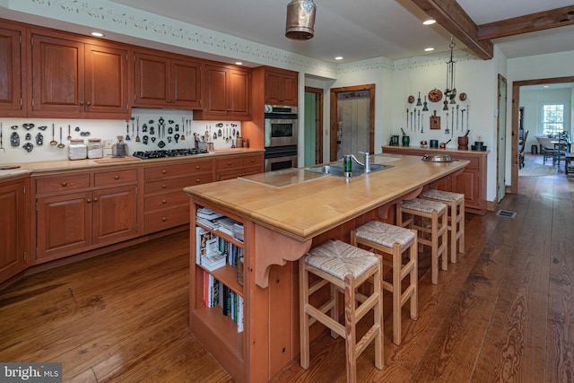 kitchen with beam ceiling, an island with sink, a kitchen breakfast bar, dark hardwood / wood-style floors, and stainless steel appliances