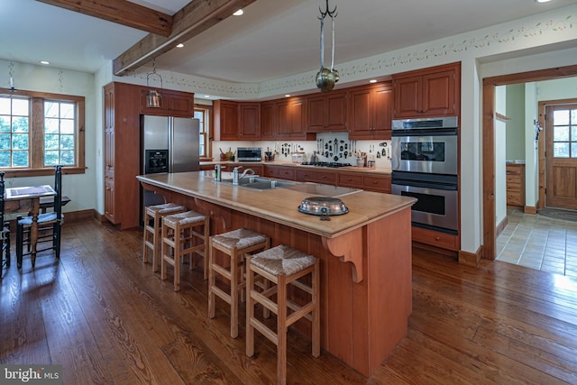 kitchen with sink, an island with sink, stainless steel appliances, and dark hardwood / wood-style flooring