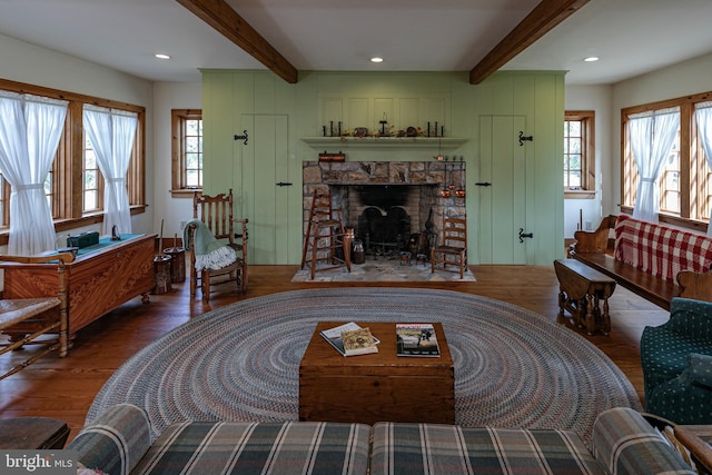 living room featuring hardwood / wood-style flooring, beamed ceiling, plenty of natural light, and a stone fireplace