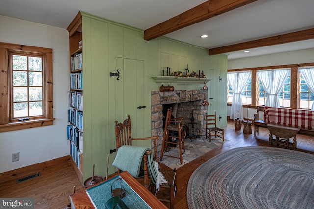 living room with beam ceiling, a stone fireplace, wood-type flooring, and a healthy amount of sunlight