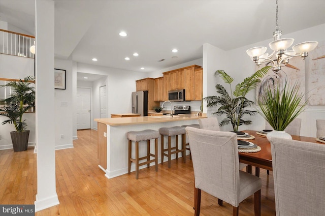 kitchen featuring appliances with stainless steel finishes, kitchen peninsula, a kitchen breakfast bar, and light wood-type flooring