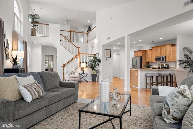 living room featuring a high ceiling, ceiling fan, sink, and light hardwood / wood-style flooring