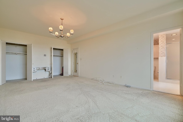 unfurnished bedroom featuring carpet flooring, two closets, and an inviting chandelier