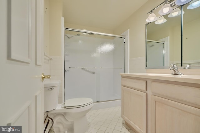 bathroom featuring tile patterned floors, toilet, a shower with door, vanity, and tile walls