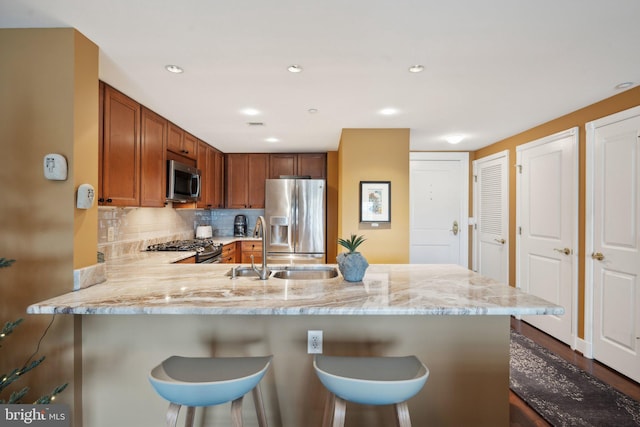 kitchen with kitchen peninsula, appliances with stainless steel finishes, a kitchen bar, and decorative backsplash