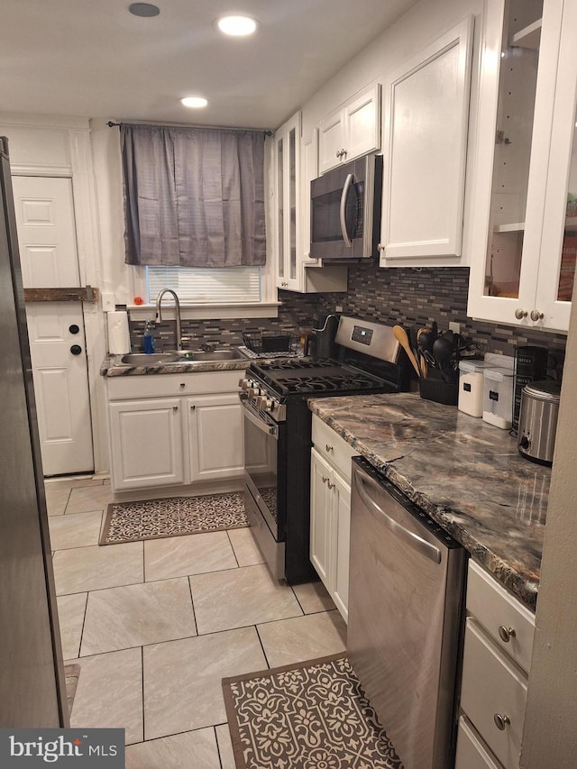 kitchen with decorative backsplash, dark stone countertops, white cabinets, stainless steel appliances, and sink