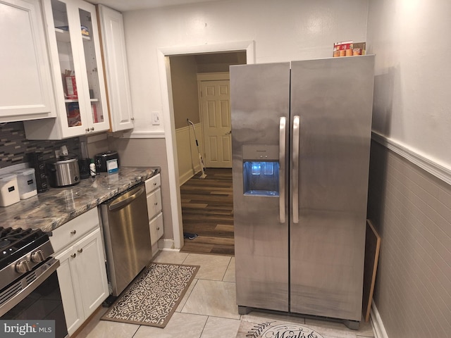 kitchen featuring appliances with stainless steel finishes, dark stone counters, white cabinetry, and light tile patterned floors