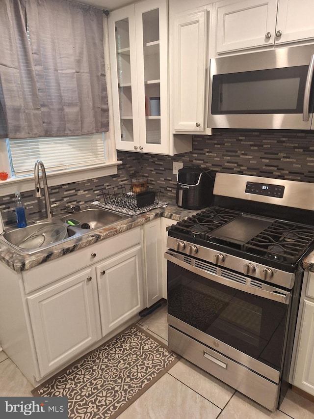 kitchen with light tile patterned flooring, sink, white cabinetry, backsplash, and appliances with stainless steel finishes