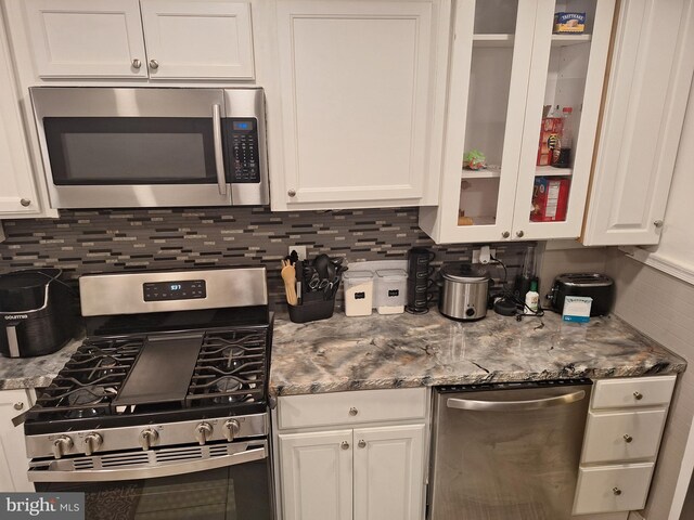 kitchen with dark stone counters, backsplash, white cabinetry, and stainless steel appliances