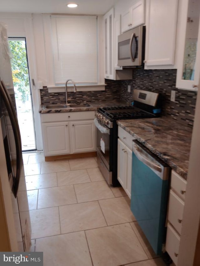 kitchen with dark stone counters, sink, white cabinetry, appliances with stainless steel finishes, and light tile patterned floors