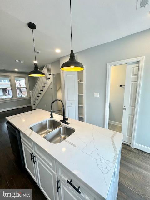 kitchen featuring a center island with sink, light stone counters, white cabinetry, dark hardwood / wood-style floors, and sink