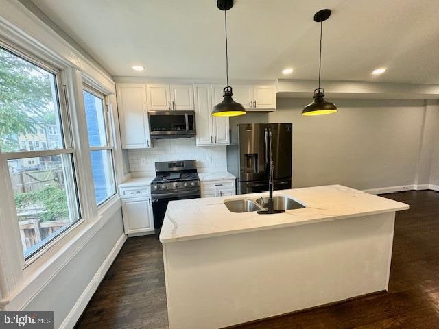 kitchen with stainless steel appliances, a center island with sink, pendant lighting, white cabinetry, and light stone counters