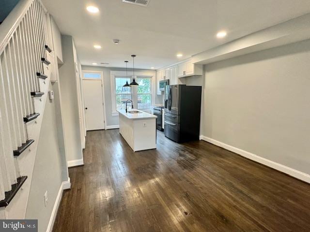 kitchen with sink, white cabinetry, stainless steel appliances, decorative light fixtures, and a center island with sink