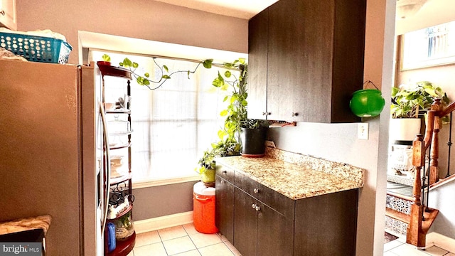 kitchen with dark brown cabinets, white refrigerator, light stone counters, and light tile patterned floors