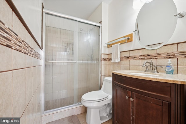 bathroom with a shower with door, vanity, tile patterned floors, toilet, and tile walls