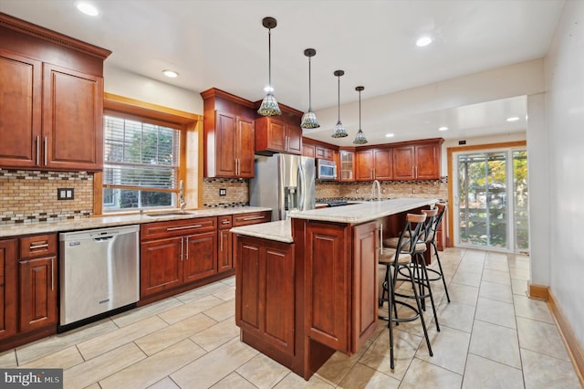 kitchen featuring stainless steel appliances, tasteful backsplash, a kitchen bar, hanging light fixtures, and a kitchen island with sink