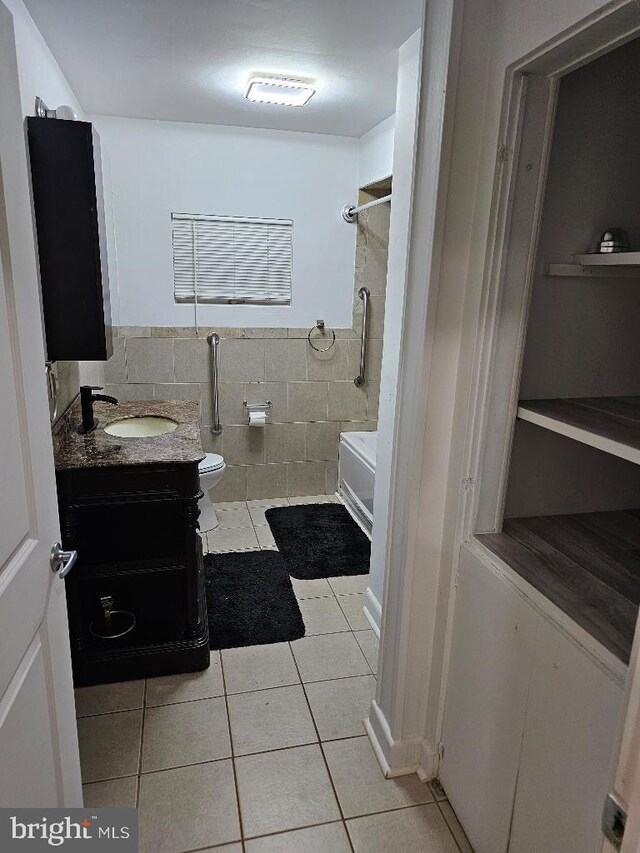 full bathroom with tile walls, tile patterned floors, washtub / shower combination, vanity, and toilet